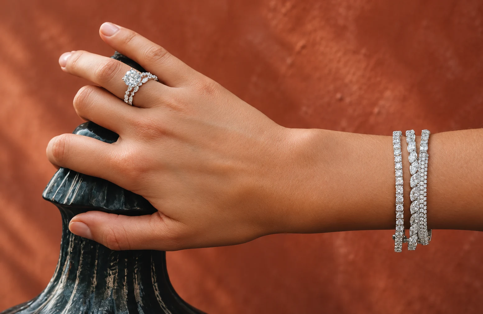 A hand wearing a ring and layered bracelets against a terracotta background